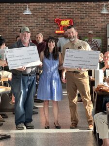 photo of a woman in a blue dress between two men who are each holding a large check